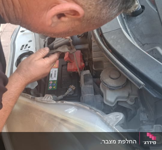 אדם בודק מצבר ברכב עם מכסה פתוח